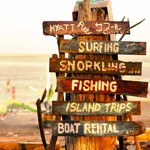 poteau en bois avec des panneaux indiquant des activités au bord de la mer : surf, snorkeling, pêche..